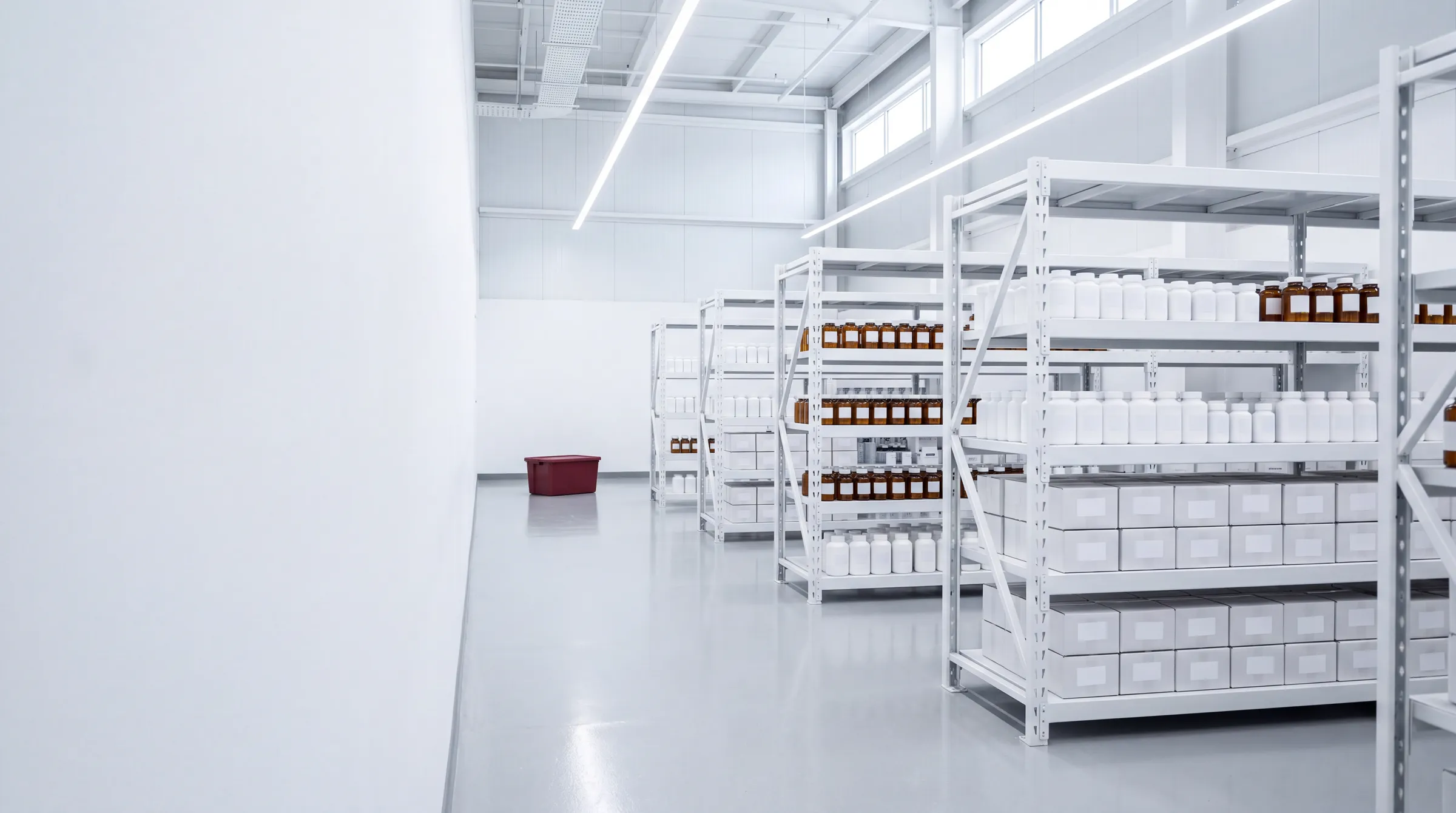 A bright warehouse aisle of white steel shelving stocked with amber and white stock bottles and white cartons